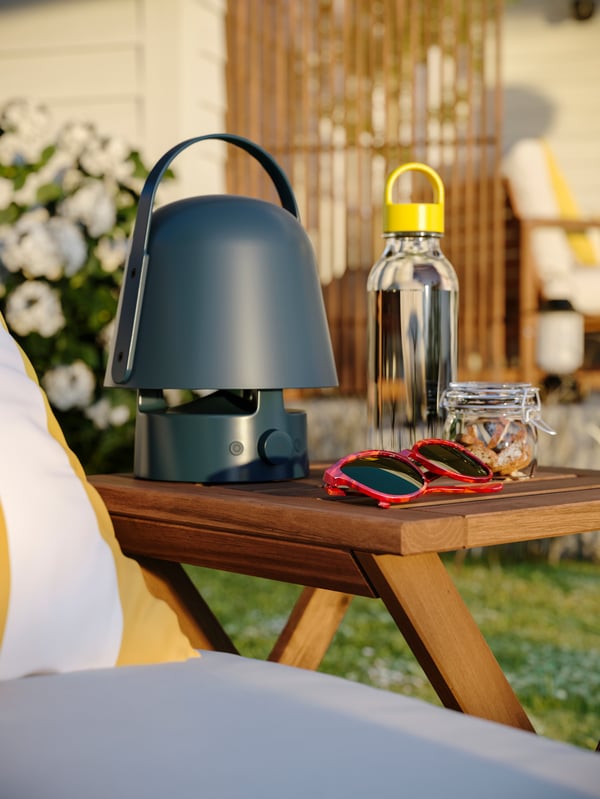 Krupan kadar NÄMMARÖ baštenske stoličice s VAPPEBY bluetooth zvučnikom-lampom, naočarima za sunce, bocom i teglom na njoj.