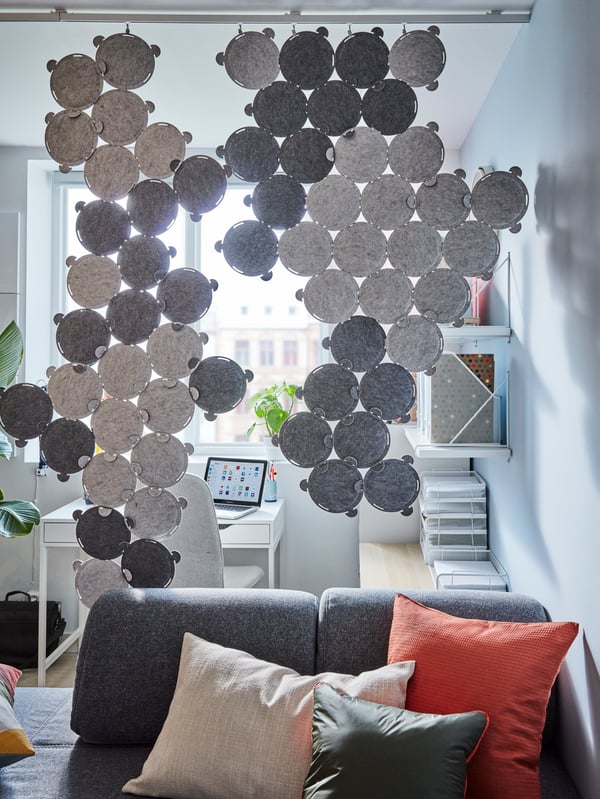 Grey sound-absorbing panels used as a room divider between a living room with a medium grey sofa and a home office.