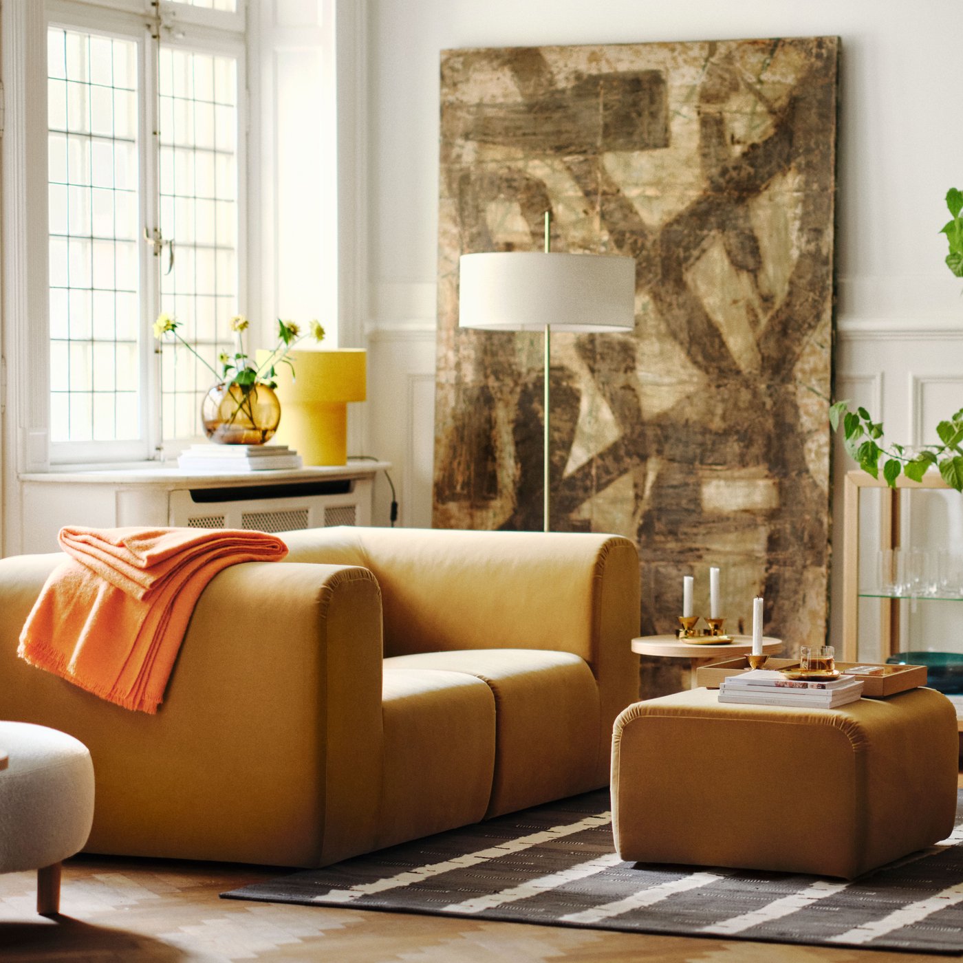 A bright living room with two beige STOCKHOLM 2025 2-seat sofas facing each other, with a pouf on a rug between them.