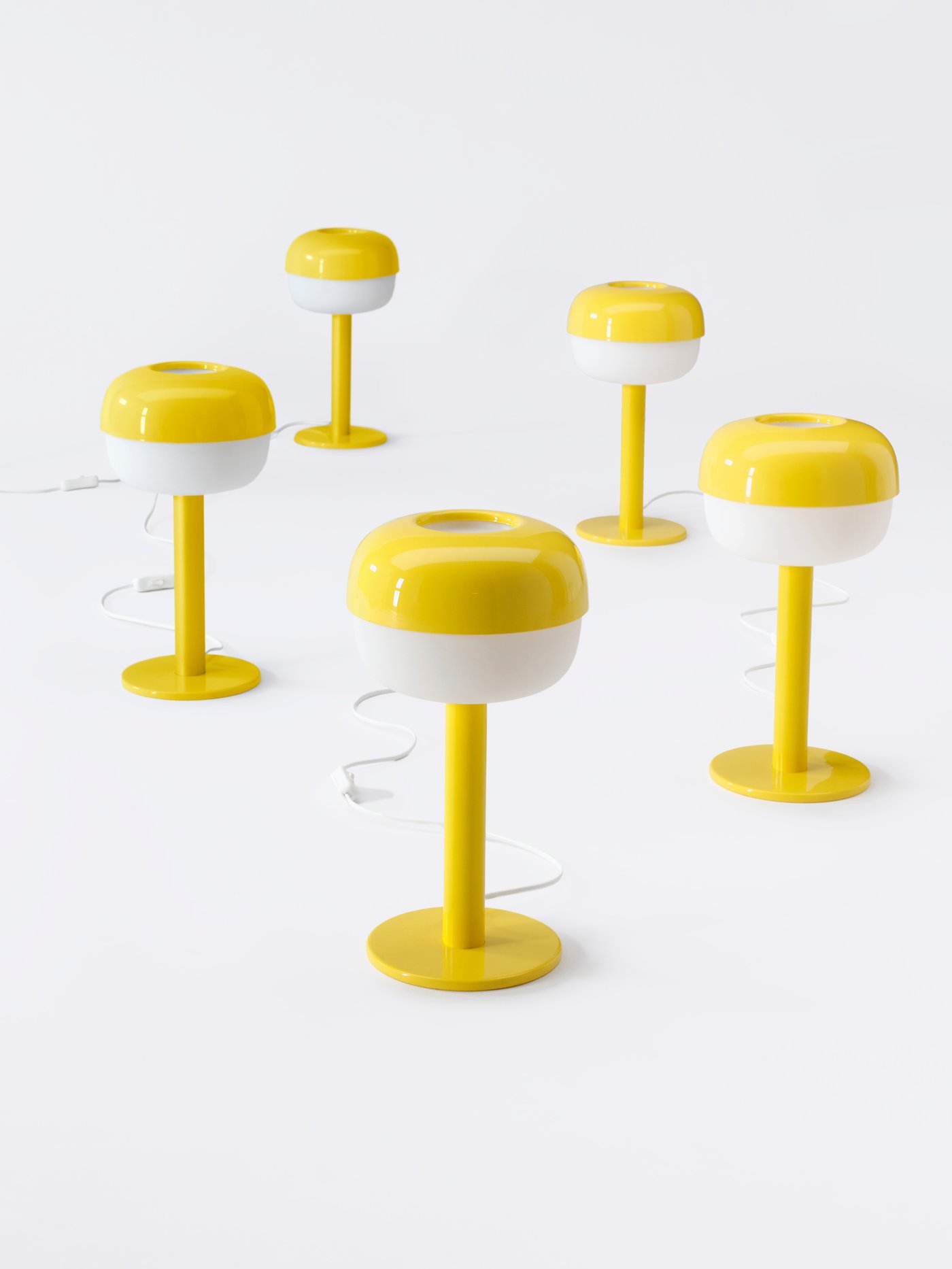 Five yellow IKEA lamps are lined up on a white floor.