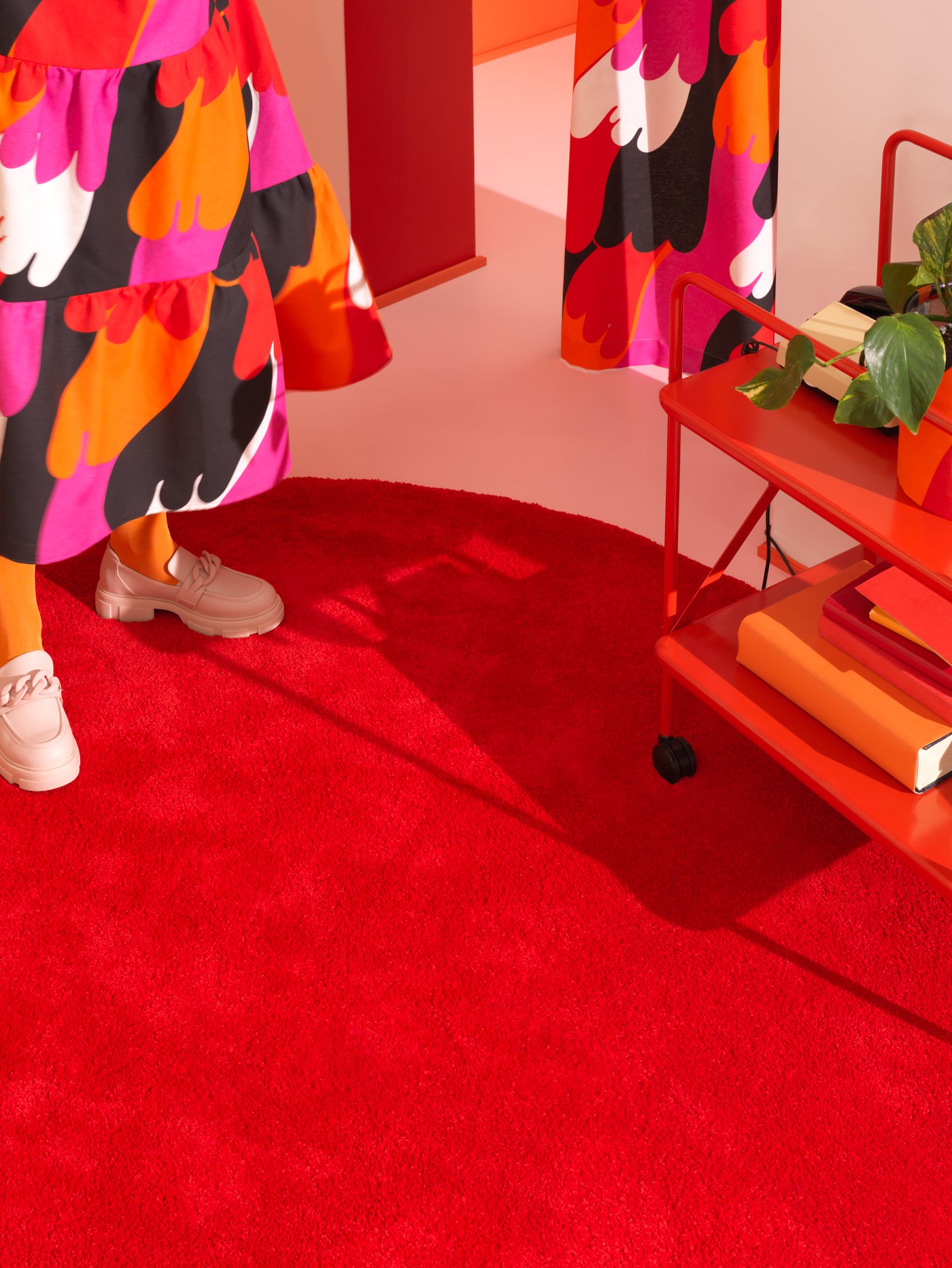 Ein runder roter IKEA Teppich ist vor einem orangefarbenen Hintergrund zu sehen.