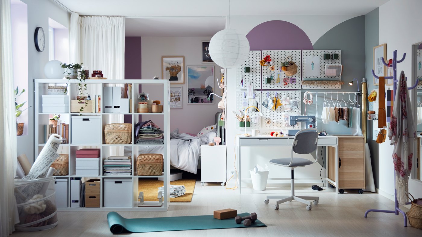 A bright, colourful room with pegboards over an ALEX desk, and curtains and a KALLAX shelving unit sectioning off a bed.