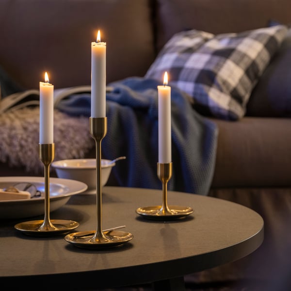 Tre mässingsfärgade ljusstakar i olika höjd med tända vita ljus.