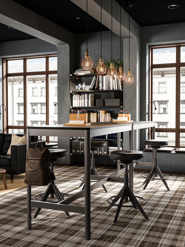 Two high tables put together, eight active sit/stand support chairs, five glass pendant lamps and shelves with books.