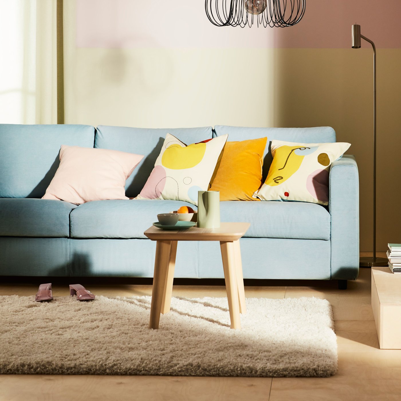 Ein hellblaues VIMLE 3er-Sofa mit bunten Kissen und einem VOLLERSLEV hochflorigen Teppich davor.