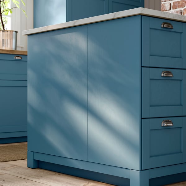 A closeup of the side of a kitchen island made of SEKTION cabinet with blue LERHYTTAN fronts, cover panels, legs and plinths.