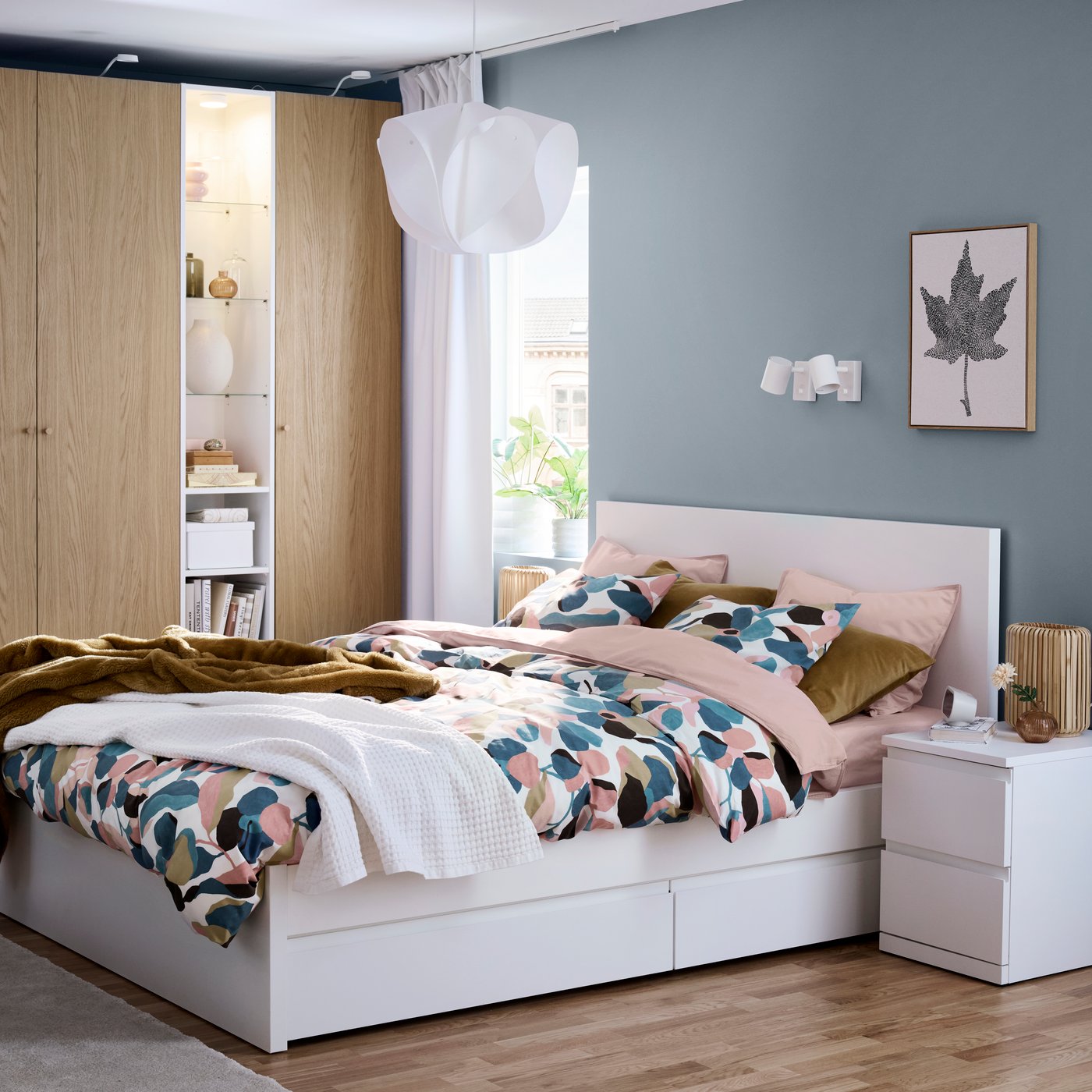 *A white STORKLINTA bed with patterned bedding in a bedroom with a blue wall and a light wood PAX wardrobe.