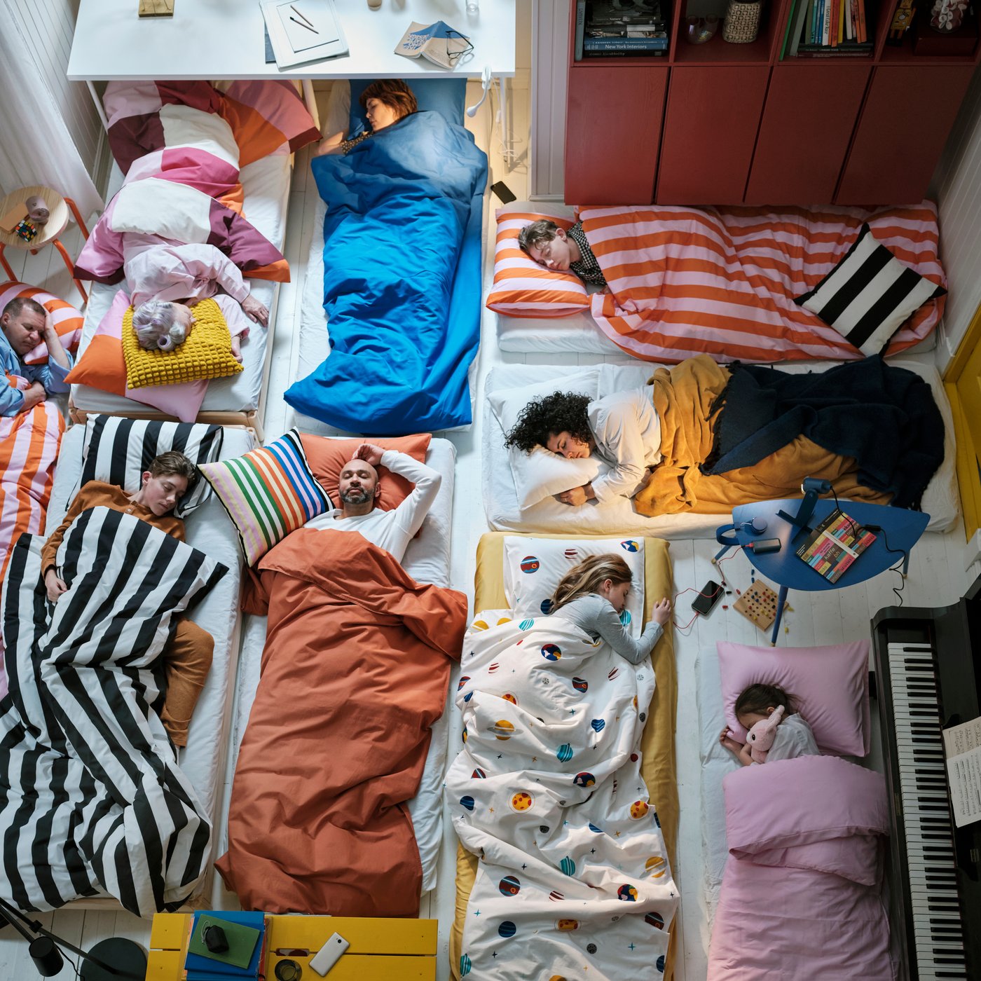 Nine people sleep on different mattresses with each having different coloured bedding, including ÄNGSLILJA duvet cover.
