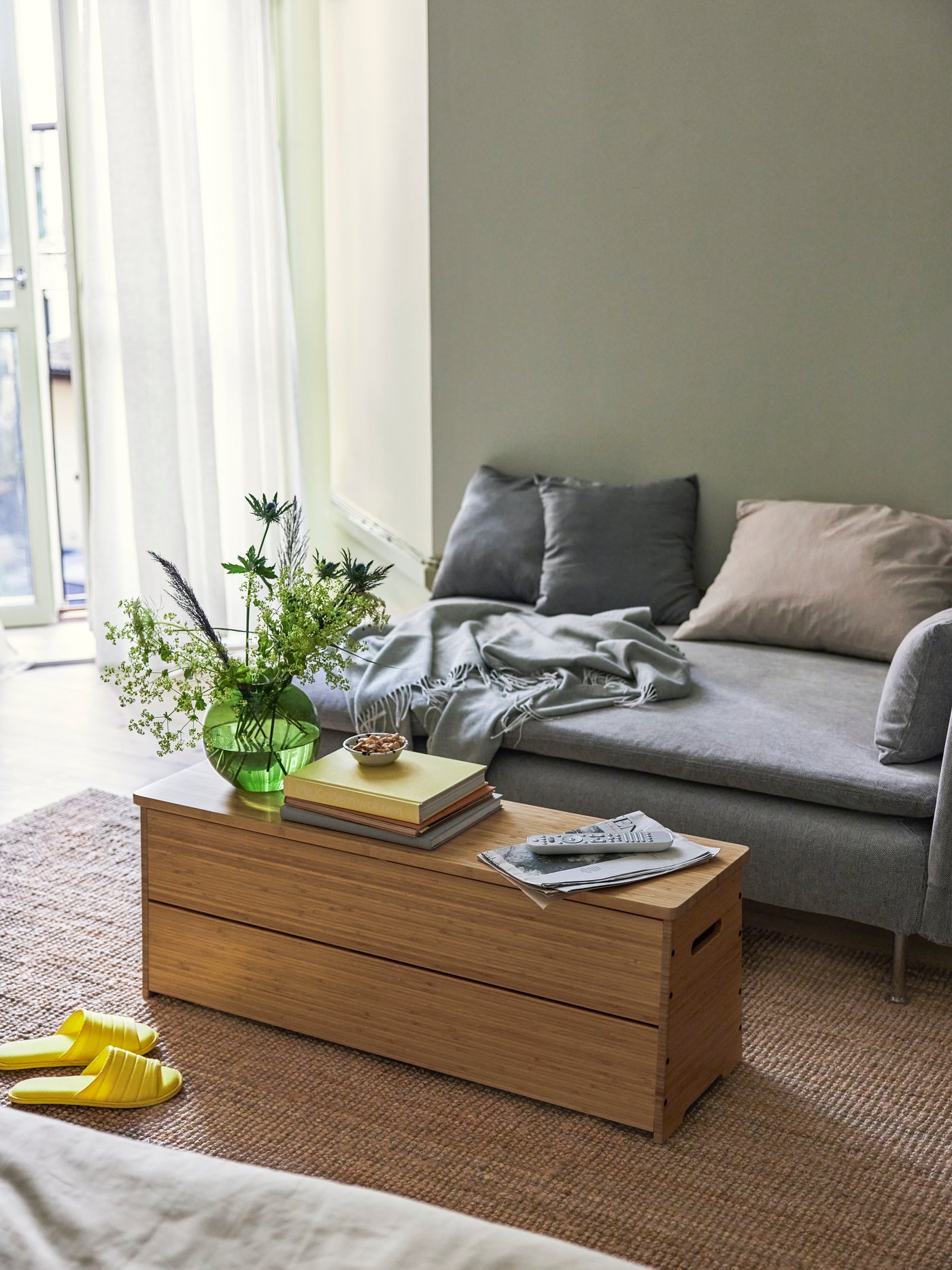 The DAJLIEN bench with storage sits neatly in front of a sofa. A vase with flowers and books are stacked neatly on top.