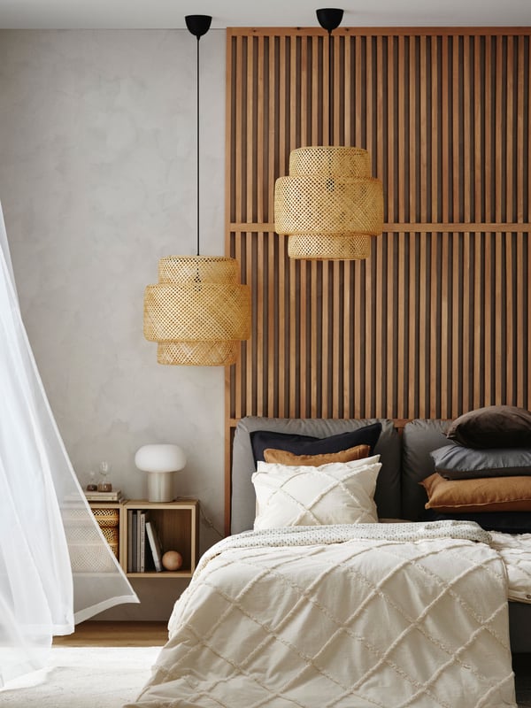 Two large SINNERLIG pendant lamps made of bamboo are hanging from the ceiling above a wooden headboard in a bright bedroom.