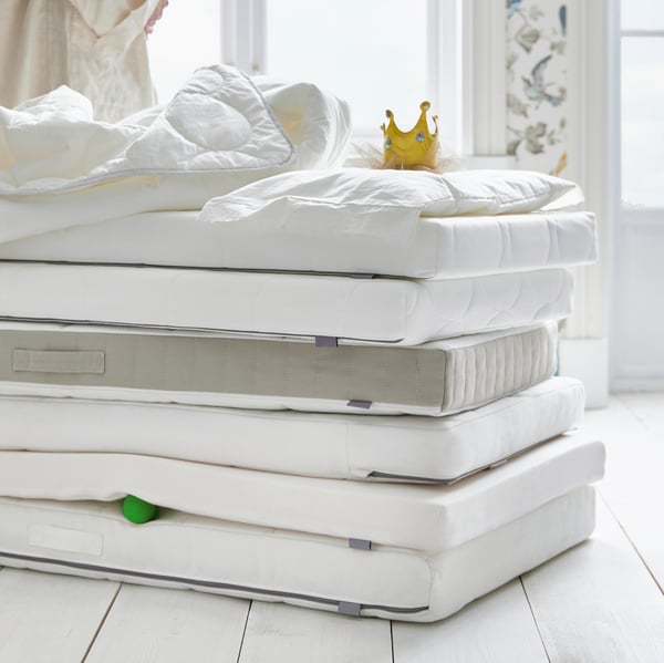 Banyak tilam katil bayi ditindan di atas lantai dengan duvet, bantal dan mahkota mainan terletak di atasnya.