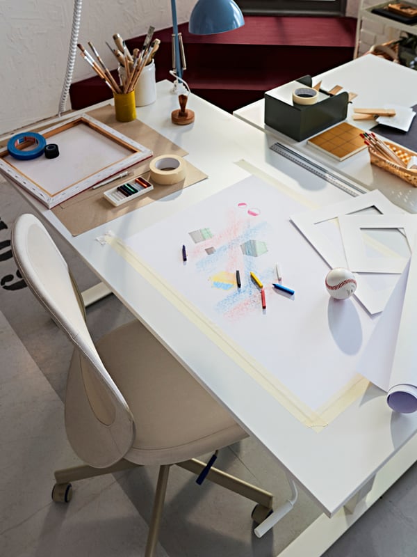 A TROTTEN desk with a FLINTAN office chair close by. The desktop has accessories, pens and paper filled with sketches.
