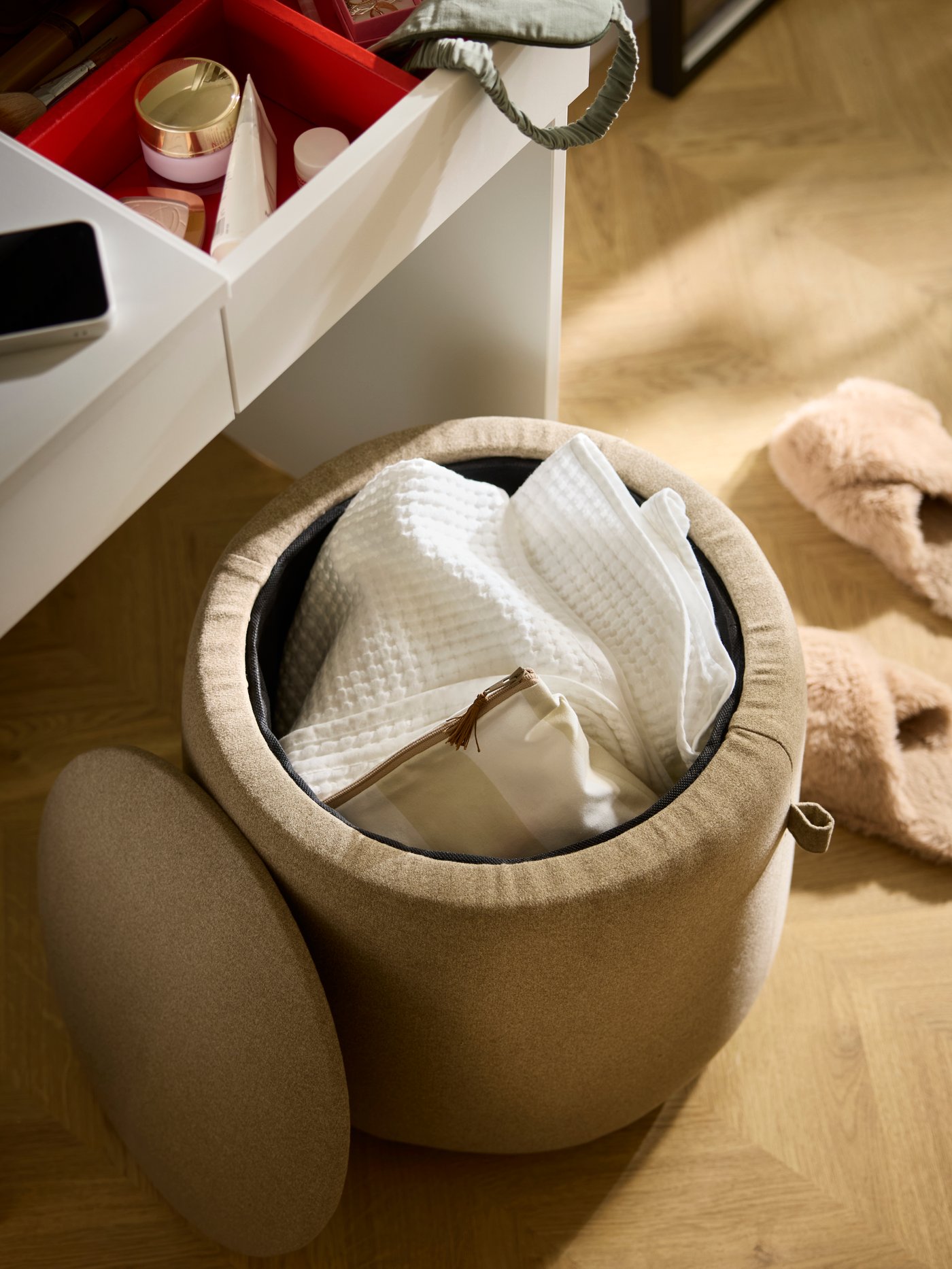 A cylinder-shaped JÄRRESTAD pouffe, its lid off revealing textiles in its compartment, placed by a BRIMNES dressing table.