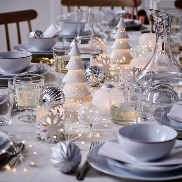 VINTERFINT decorations and STRÅLA lighting are on a festively decorated dinner table in tones of white and silver.