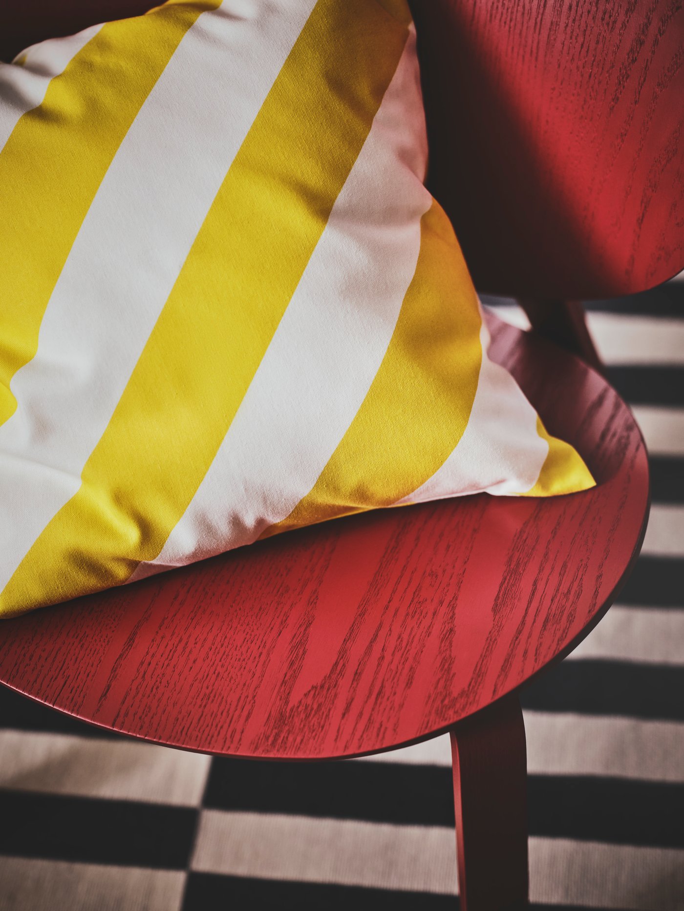 A close-up of a red chair with a yellow and white stripey cushion on top. Underneath is a black and white striped rug.