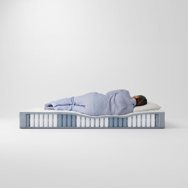 The side view of a VALEVÅG pocket sprung mattress that is cut out, showing its individual pocket springs. A person is on top.