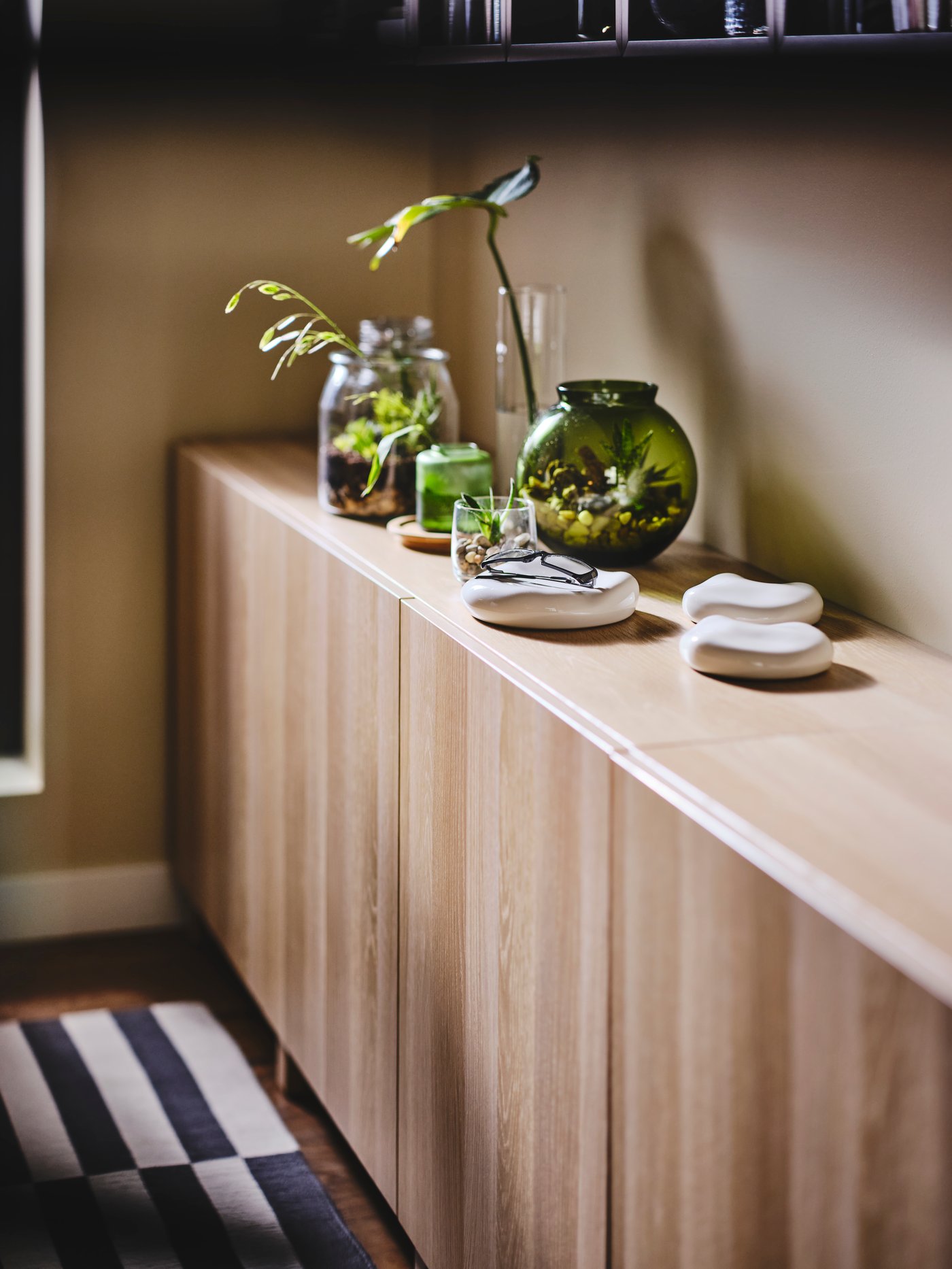 A BESTÅ cupboard with a green KONSTFULL vase and other accessories in the living room.