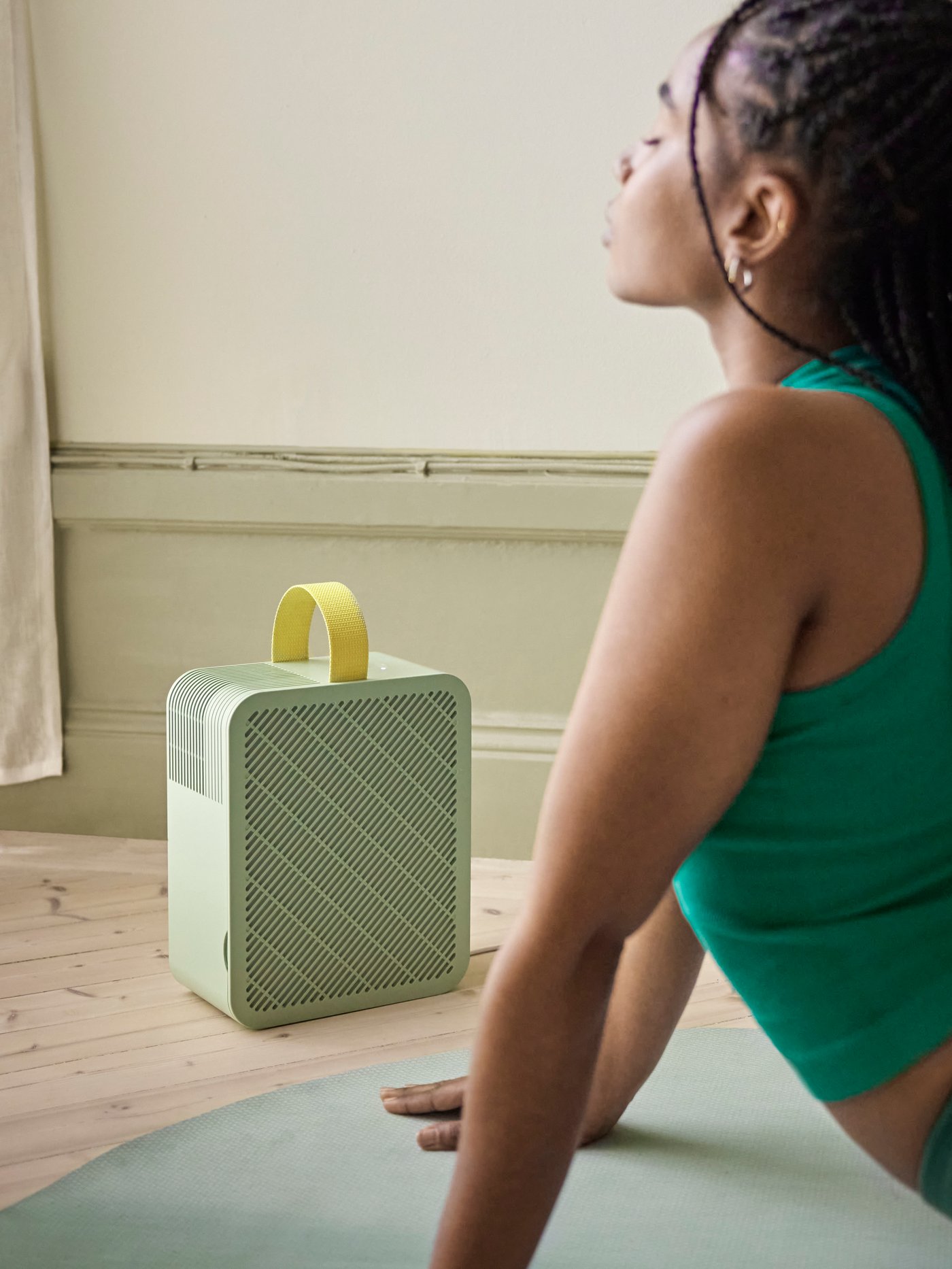 A woman is stretching on her stomach on a DAJLIEN exercise mat, eyes closed, with the DAJLIEN air purifier in front of her.
