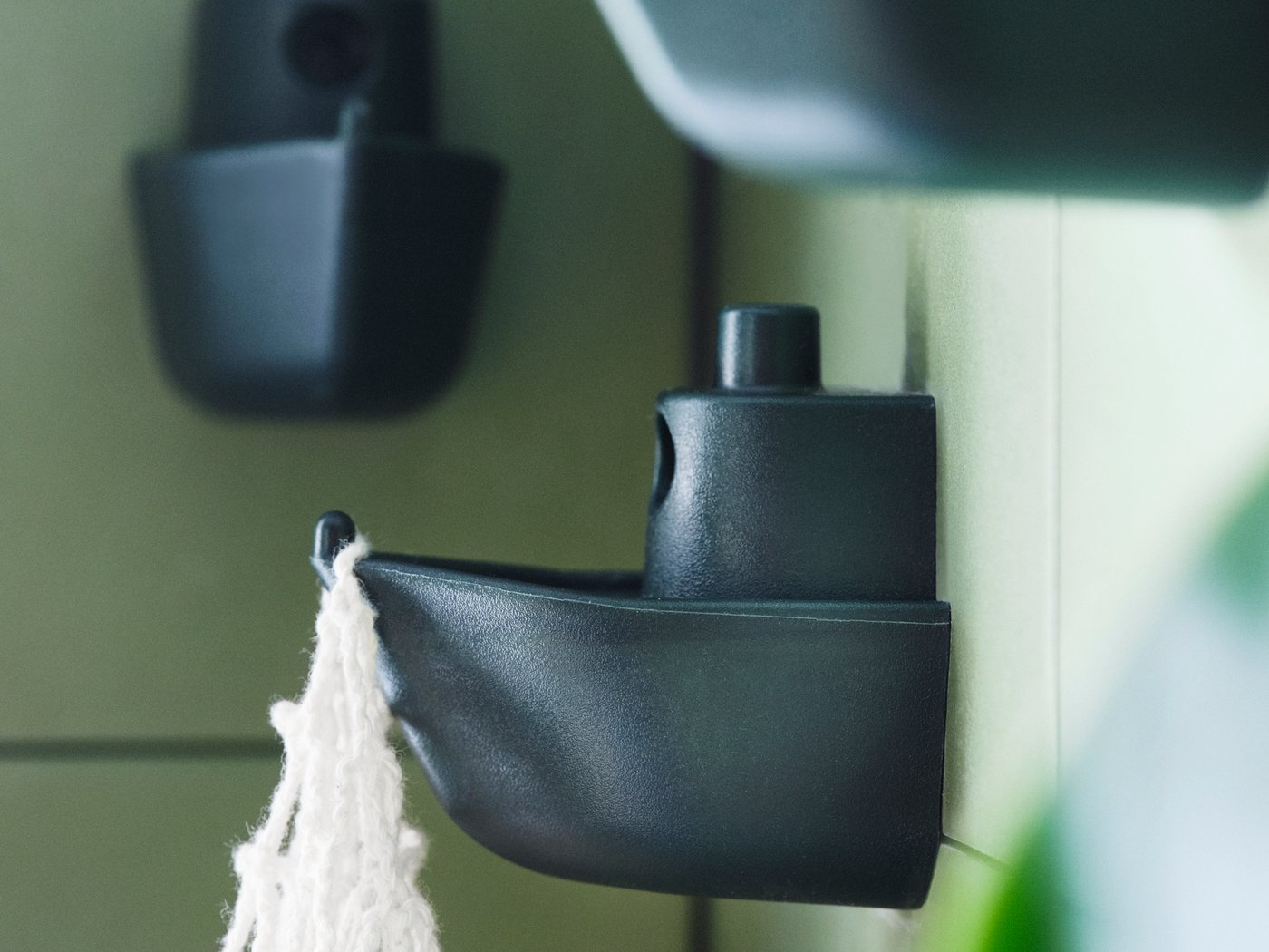 Drei an der Wand montierte KNOPARE Haken sind in unterschiedlichen Höhen angebracht. An einem hängt eine weisse Macramé-Tasche.