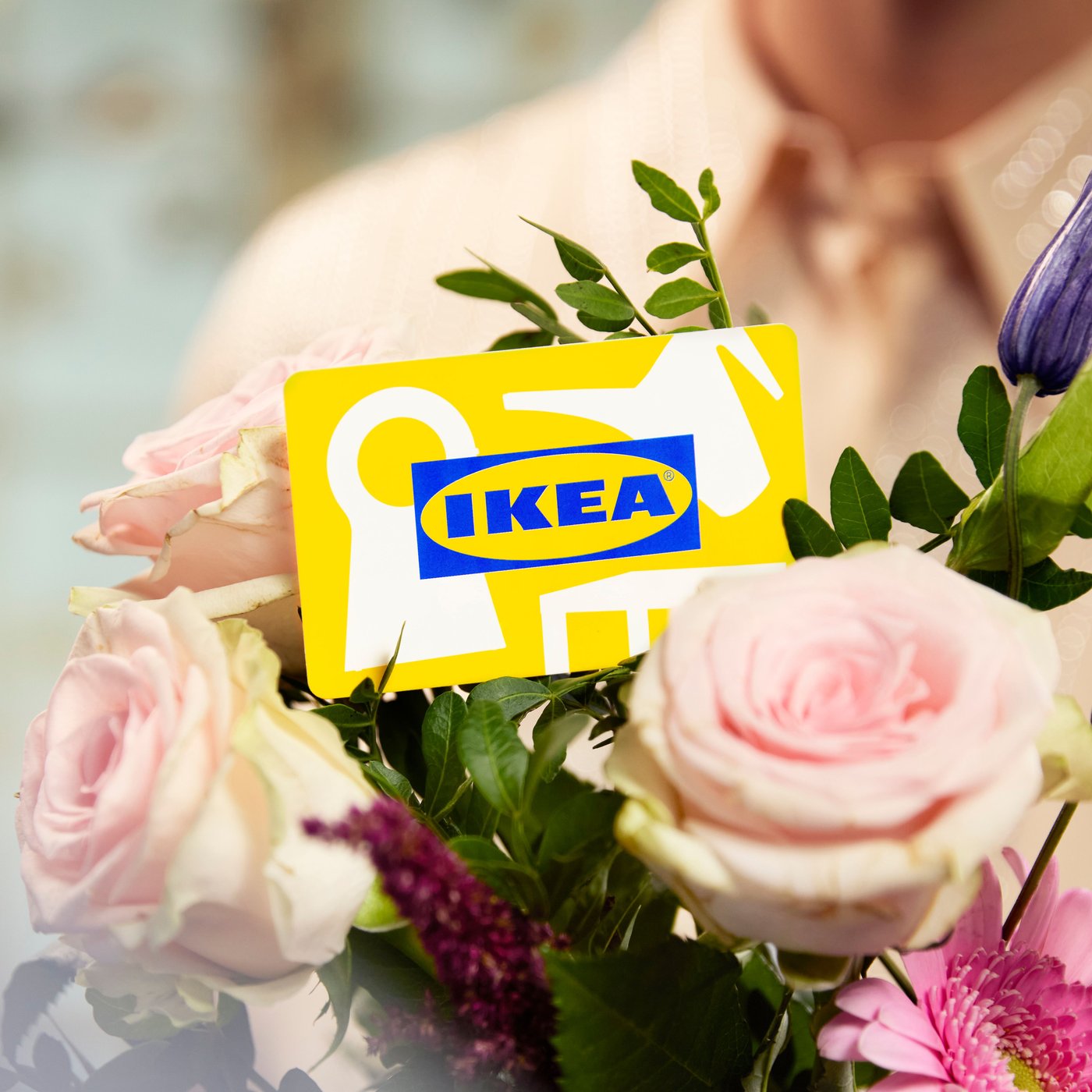 Darilna kartica IKEA v šopku cvetja, v ozadju oseba.