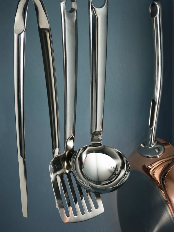 FINMAT kitchen utensils and pan hanging against a blue wall.