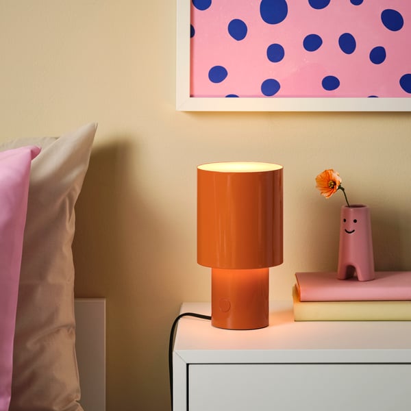 Eine dimmbare, orangefarbene SPETSBOJ-Tischlampe steht auf einem Nachttisch im Schlafzimmer