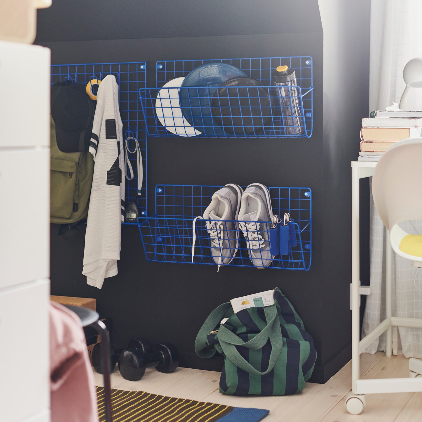 Ein Sportbereich mit GREJIG Wandaufbewahrungen, die an einer dunklen Wand montiert sind. Darin sind Schuhe, Frisbee-Scheiben und eine Tasche aufbewahrt.