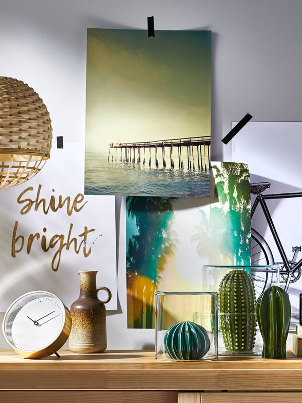 Une commode en bois derrière laquelle sont accrochés trois cactus et différents tableaux.