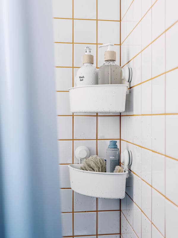 Two white corner shelf units with suction cups holding shampoo and shower gel bottles, and a bath sponge.