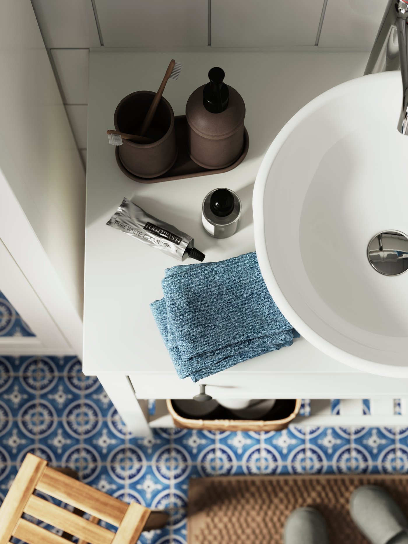 An ÅLTJÄRN bathroom set, with a toothbrush holder and a soap dispenser on a tray, is standing on a white HEMNES wash-stand.