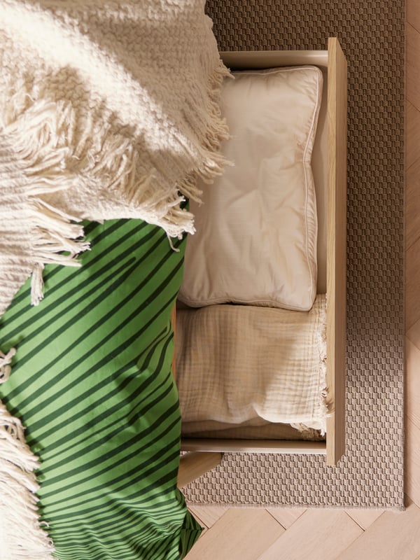 Bild tagen uppifrån på en säng med grönrandig påslakan, vita kuddar och beige matta.