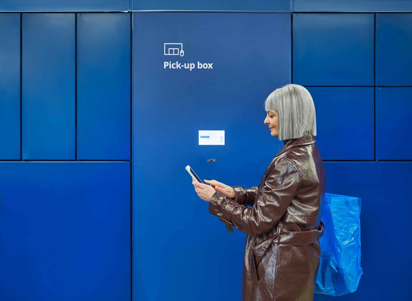Una donna è davanti a un locker IKEA con scomparti di diverse dimensioni e controlla il suo numero di ritiro sullo smartphone