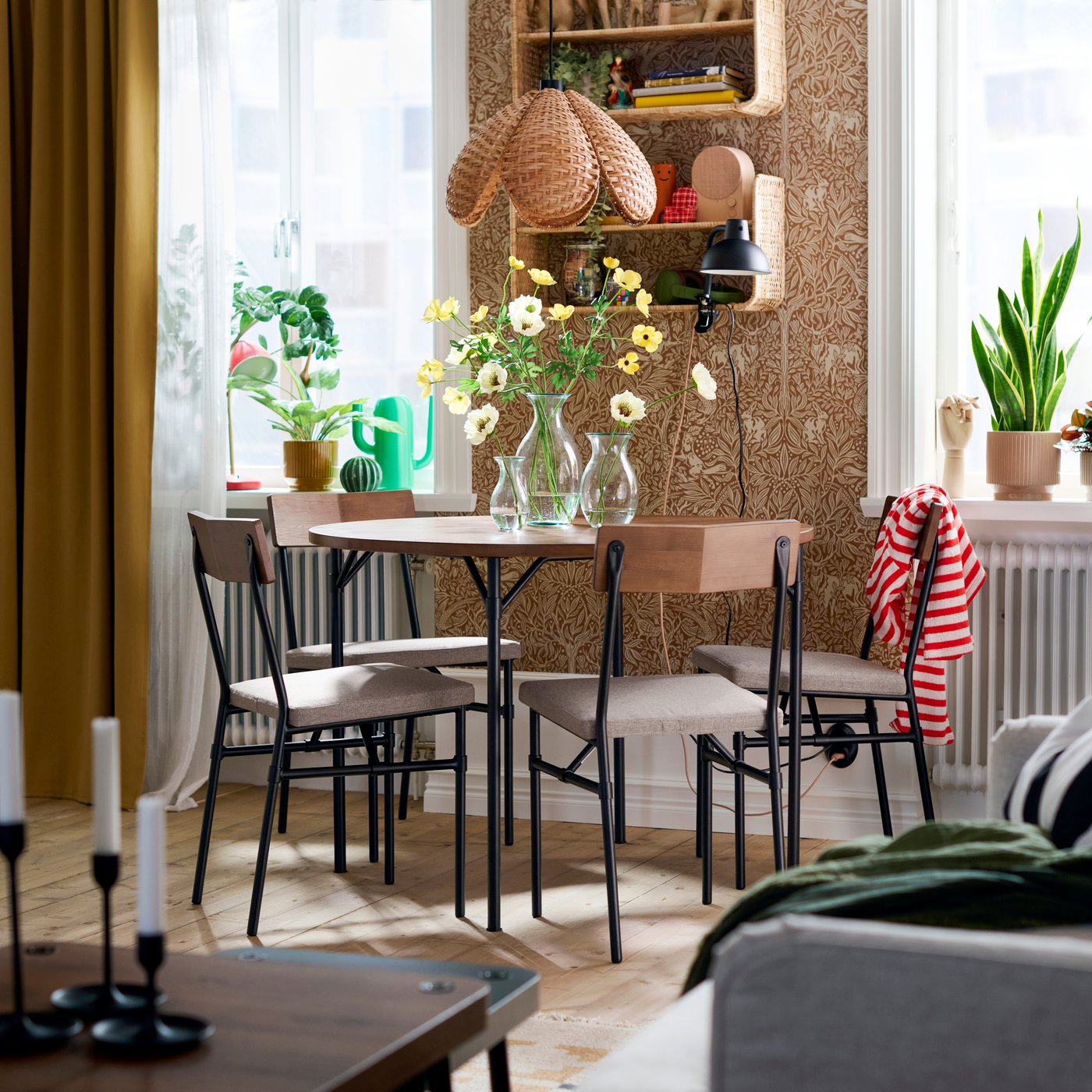 Espace repas équipé de quatre chaises GRÖTÅN en Tibbleby beige foncé entourant une table en bois ornée de fleurs et surmontée de tablettes.