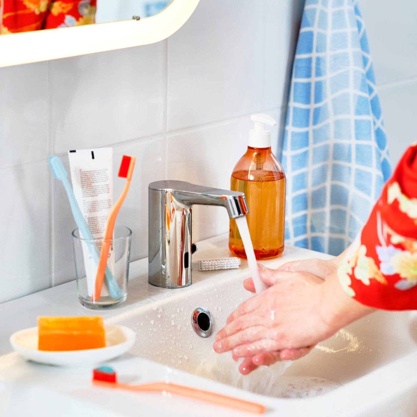 Personne se lavant les mains à un mitigeur pour lavabo avec capteur BROGRUND, entouré de brosses à dents colorées et d’un savon.