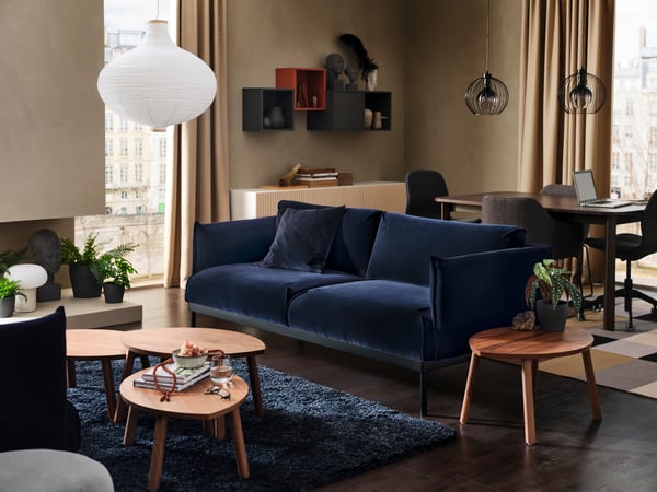 Un grand canapé en velours bleu foncé avec un canapé à deux places et plusieurs tables d’appoint, un tapis à poils hauts et des murs beiges.