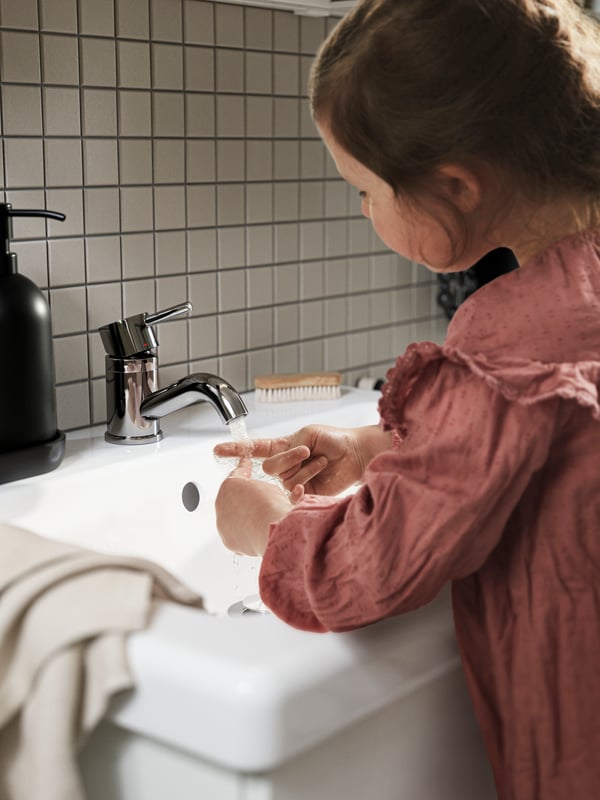 A girl washing her hands in a TVÄLLEN sink single, with a PILKÅN sink mixer tap, chrome-plated, and a hand towel.