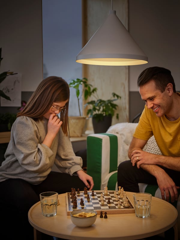In a living room, a preteen girl and her father play chess. A NÄVLINGE pendant lamp provides overhead light for their game.