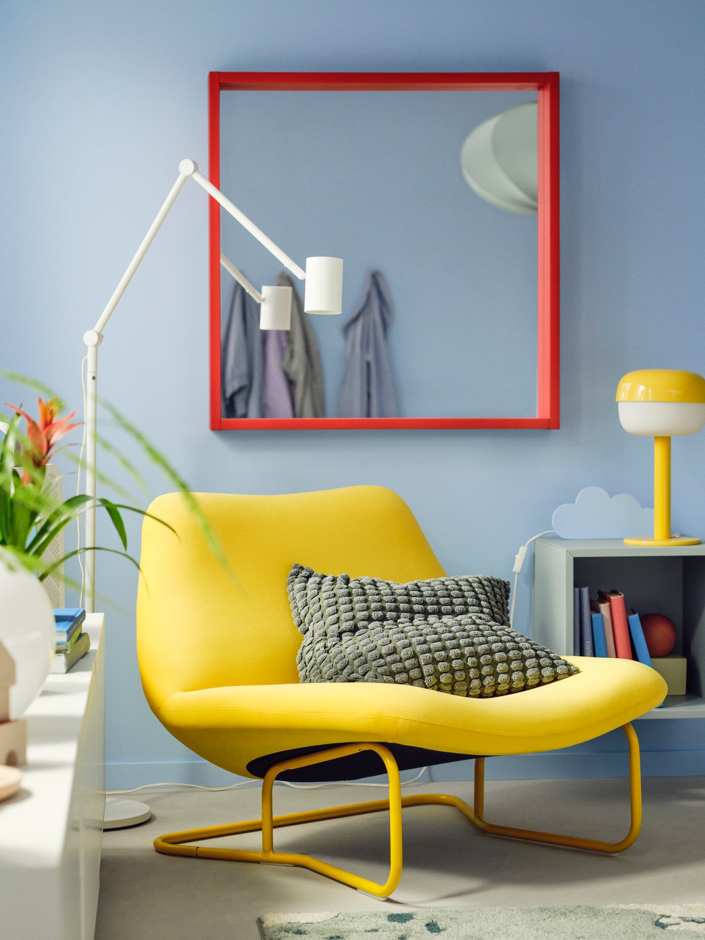 A colourful interior style with a yellow chair and red mirror on the blue wall.