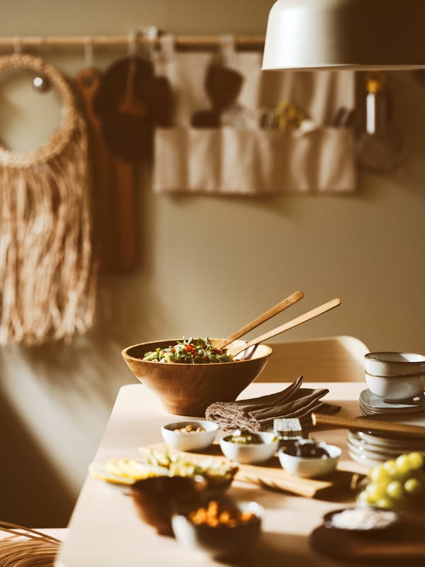 A pair of GRÖNSAKER salad servers set in a serving bowl, with three bowls placed on a tray to the side, all set on a table.