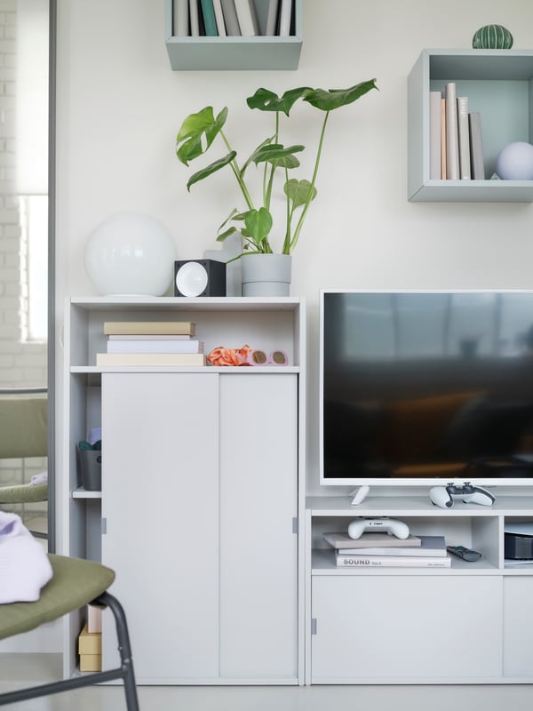 Une armoire EKET est fixée au mur au-dessus d’un téléviseur posé sur un meuble télé SPIKSMED, près d’une armoire SPIKSMED.