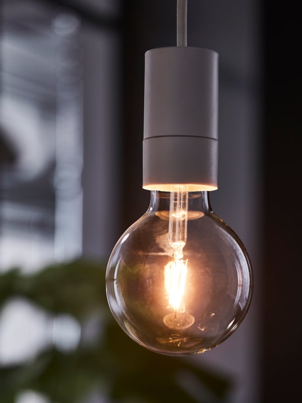 Upaljena LUNNOM E27 LED sijalica – 150 lumena, 95 mm, bistra kugla – visi s belog tekstilnog SUNNEBY seta kablova.
