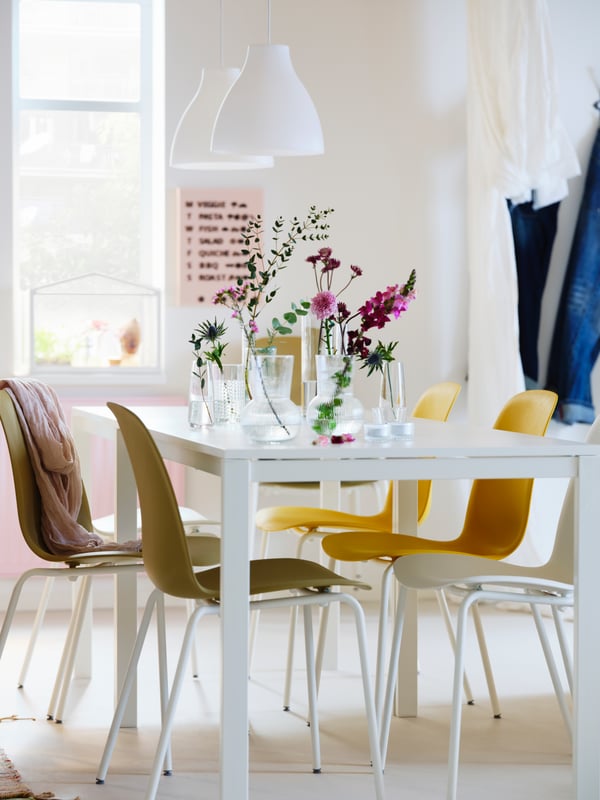 A MELLTORP dining table with yellow dining chairs around it, decorated with PÅDRAG vases with flowers.