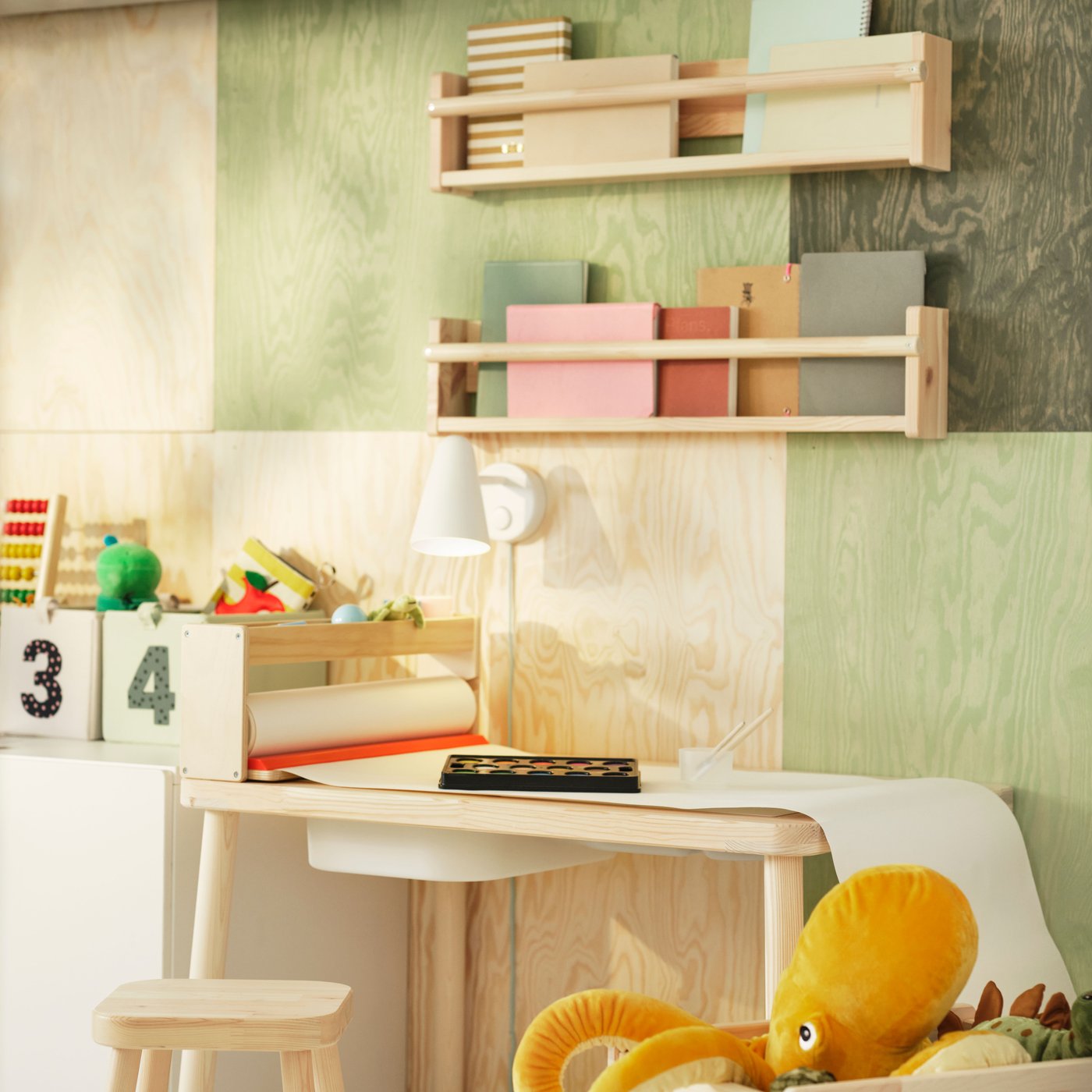 A pine FLISAT children’s table with a TROFAST storage box in its top stands under some FLISAT wall storage on the wall.