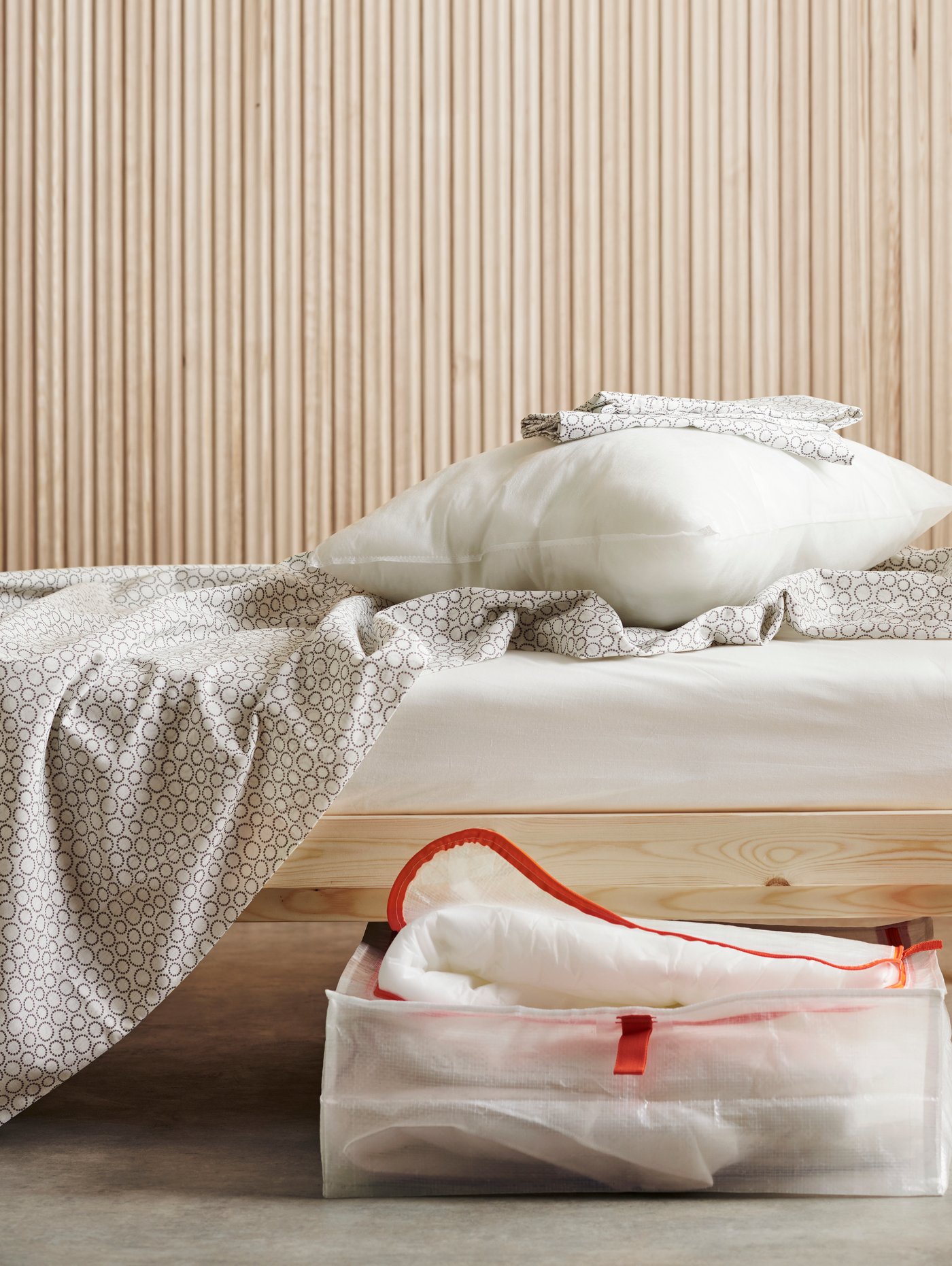 A wooden bed frame with bedding on top and a storage box with a duvet in it halfway out from under the bed.