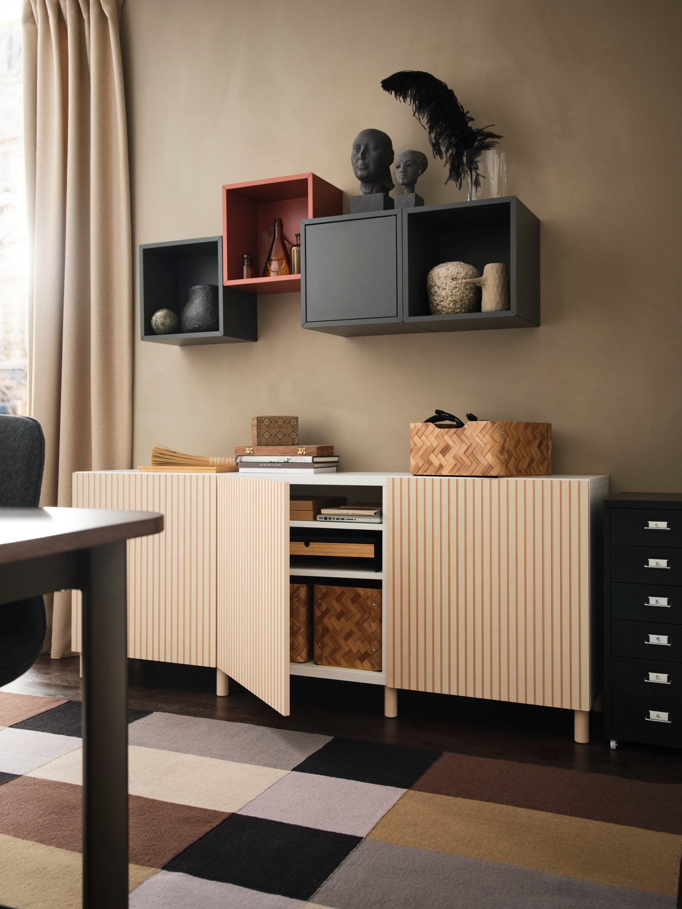A living room with a BESTÅ sideboard with wooden doors against a wall with EKET cabinets mounted on it.
