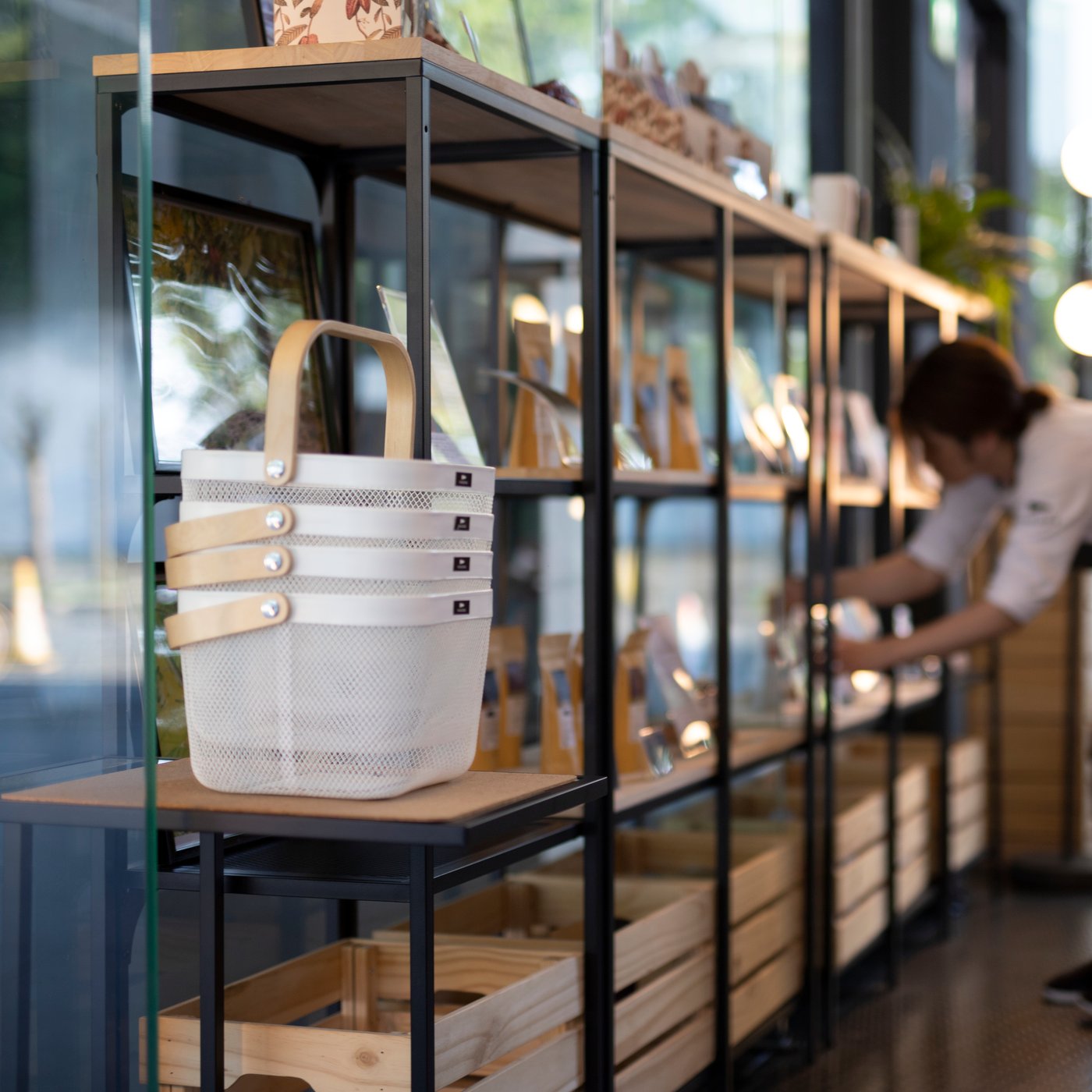 A black shelving unit with a shop owner straightening bins and containers on its shelves