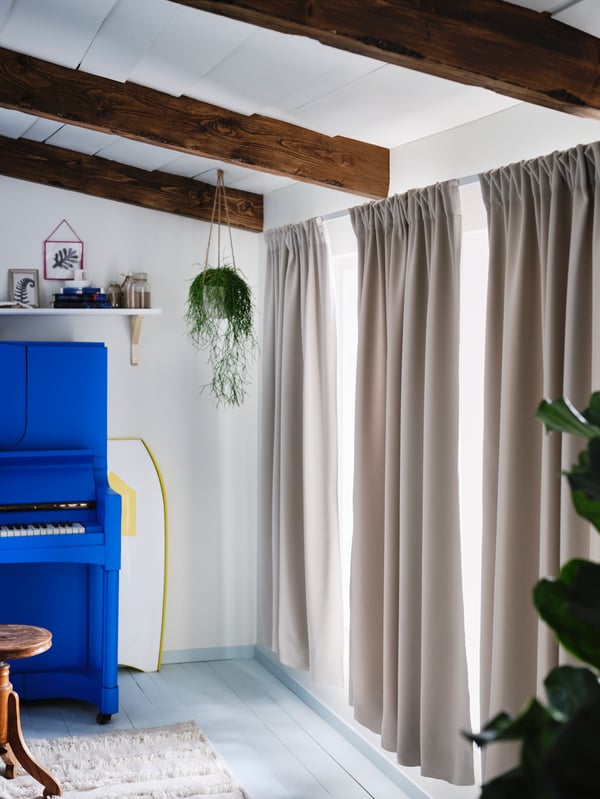 Un pianoforte accanto a delle finestre semi-coperte da tre tende in tessuto oscurante MAJGULL grigio chiaro/beige - IKEA
