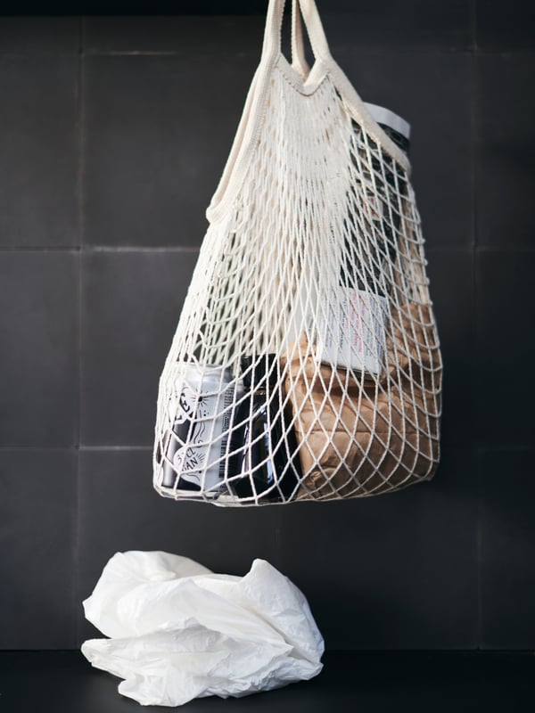 A KUNGSFORS net bag holds an assortment of groceries, while a disposable plastic bag is cast aside.