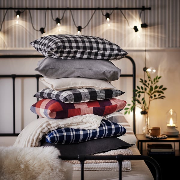 Grande pile d’oreillers sur un lit STJÄRNÖ, tous dans des couleurs chaudes comme le bleu foncé, le rouge foncé et le beige chaud.