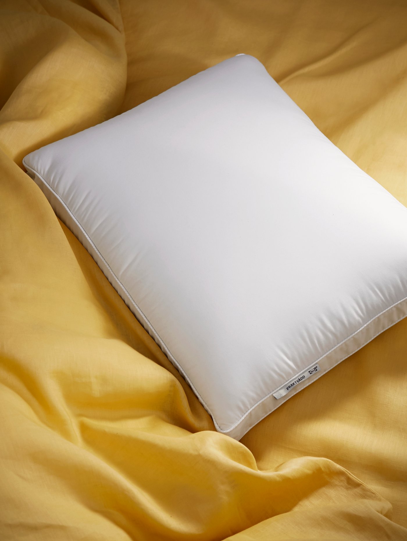 A PRAKTVÄDD ergonomic pillow on a bed on top of yellow bed linen.